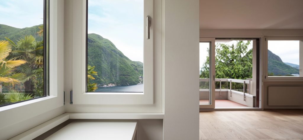 Modern interior with large windows and a sliding glass door overlooking a balcony, green hills, and a lake outside—learn why your interior doors might be warping and what to do about it for lasting beauty in every room.