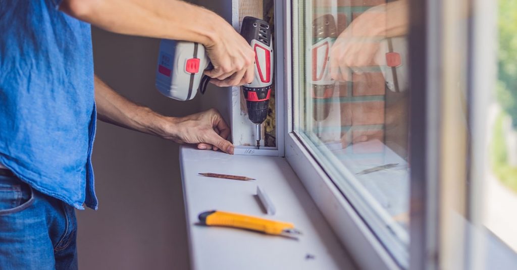 Person using a power drill to install or repair a window frame, with a utility knife and pencil on the windowsill—showing how window installation affects energy bills in Calgary homes.